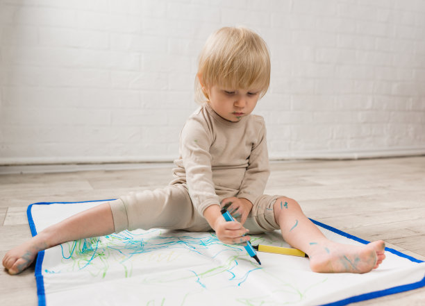 一个穿着睡衣的快乐的小女孩坐在地板上，用毡尖笔在特制的油布上画画。这张脸被油漆弄脏了图片下载