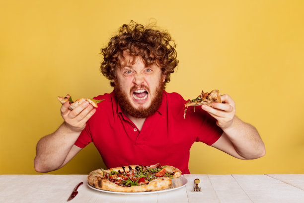 红胡子男人的肖像准备吃美味的意大利披萨孤立在黄色的工作室背景。图片下载