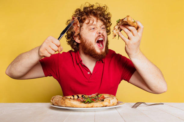 多毛的红胡子男人吃着美味的意大利披萨，被画室的黄色背景隔开。世界披萨日概念。图片下载
