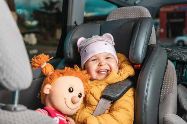照片中，一个面带微笑的白人小孩坐在儿童座椅上，手里拿着毛绒玩具。查看汽车内部。儿童公路旅行安全概念图片下载