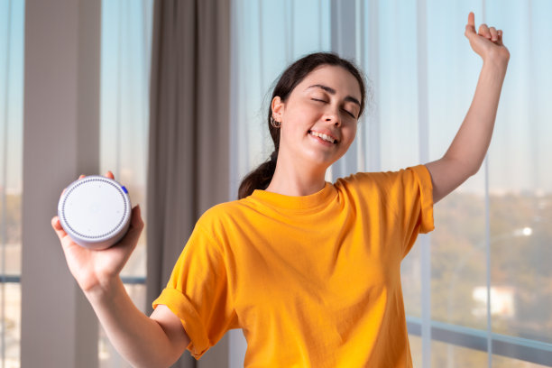 一个年轻快乐的白人女孩跳舞的肖像，拿着一个可以播放音乐的便携式智能扬声器。现代小玩意和娱乐的概念图片下载
