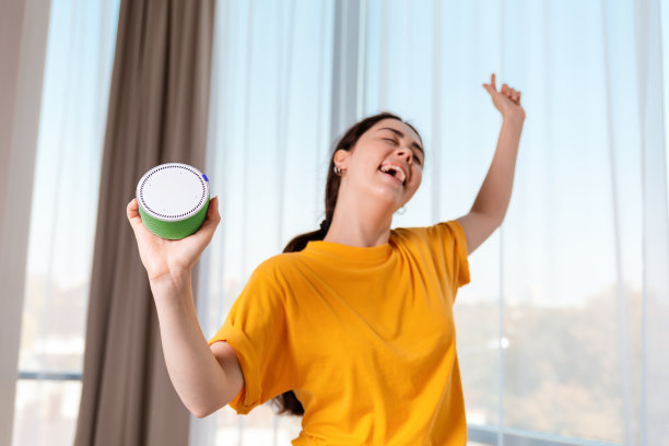 一个年轻快乐的女人跳舞的肖像，拿着一个可以播放音乐的便携式智能扬声器。现代小玩意的概念图片下载