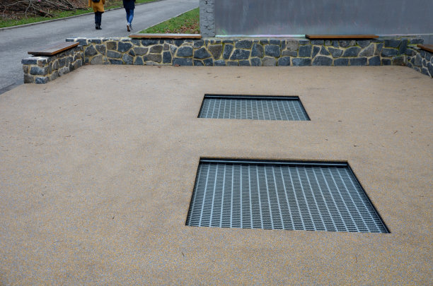 在学校操场的院子里，三个蹦床跳垫被埋入一个特殊的橡胶表面以下。四周是贴在石墙上的木凳，后院风景如画图片下载