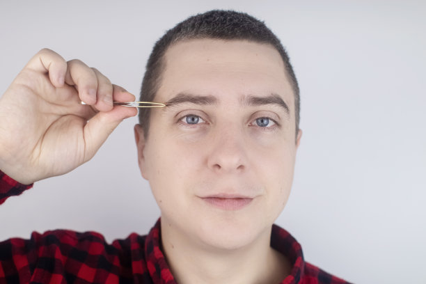 人拔眉毛。用镊子去除多余毛发的特写镜头。孤立的白色背景。一个男性看着镜框，感觉就像在看镜子一样图片下载