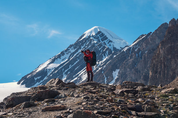 到山区进行极限探险。旅行摄影师在高高的雪山上拍摄了一张站在美丽的风景顶端的照片。旅行自由职业者，户外探险旅行概念。图片下载