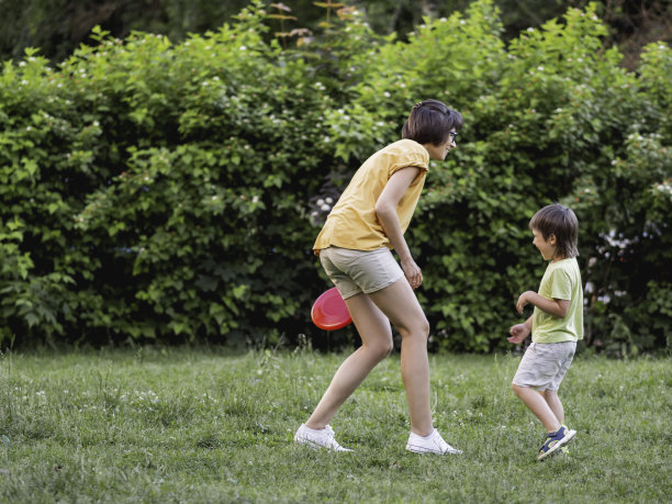 母亲和儿子在草坪上玩飞盘。夏天的氛围。户外休闲活动。家庭生活。在后院做运动。图片下载