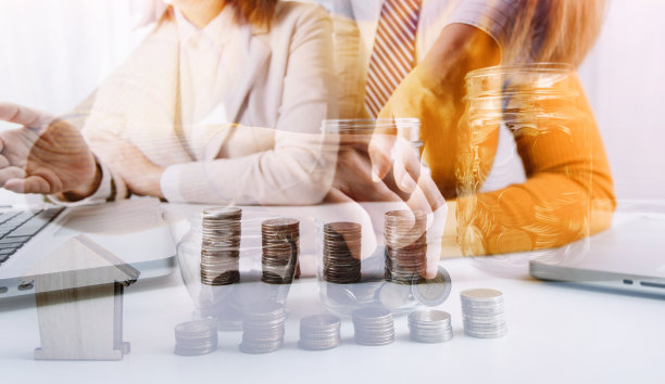 商务人士在办公桌上工作，带着存钱罐。企业金融储蓄和投资理念。手把硬币放进储蓄罐里，存钱致富。素材图片