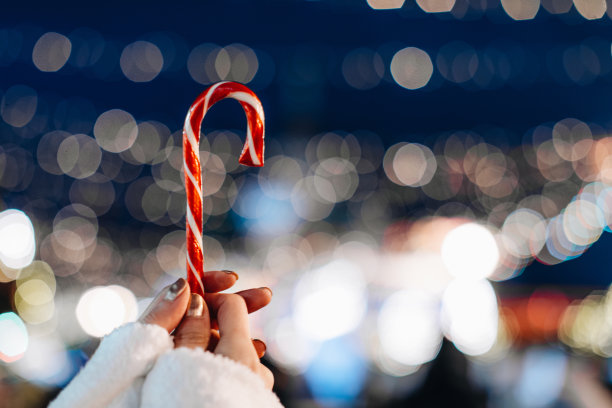 女性的手握着红白的甘蔗糖棒棒糖，背景是蓝色的银色魔法照明。图片下载