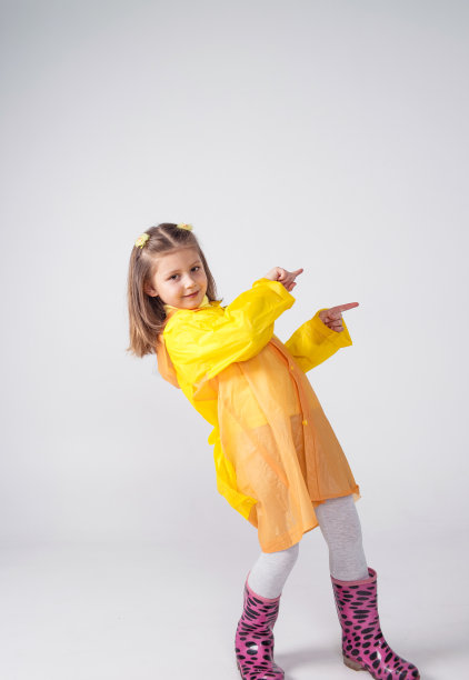 一个美丽的小女孩的肖像，在黄色雨衣上显示的手的一边孤立在白色的背景上。图片下载
