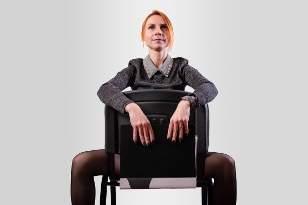 女商人，两腿叉开，向后坐在椅子上，背景是灰色的图片下载