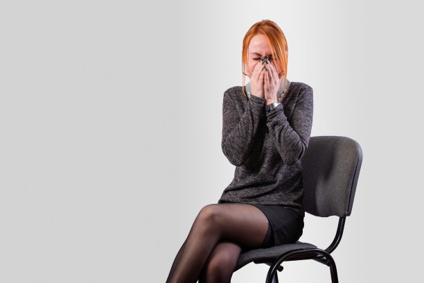 一个穿着工作服的女孩用手捂着脸，在灰色的背景上哭泣图片下载