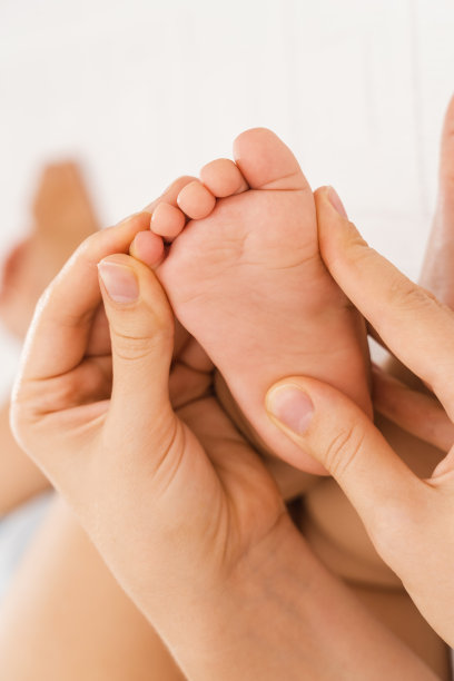 妈妈为熟睡的宝宝做足底按摩，妈妈的手轻轻按摩新生的脚部。垂直与图片下载