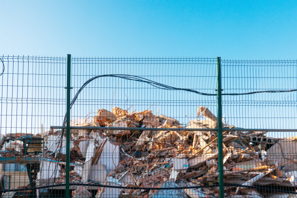 围栏后面是一座被摧毁的建筑物的废墟。蓝色的天空。底部视图。拆除建筑物的概念图片下载