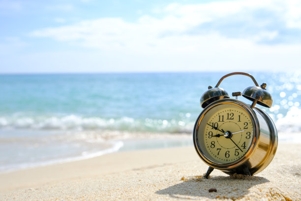 新的一天的早晨，沙滩上的清晨阳光下的闹钟。健康的概念。图片下载