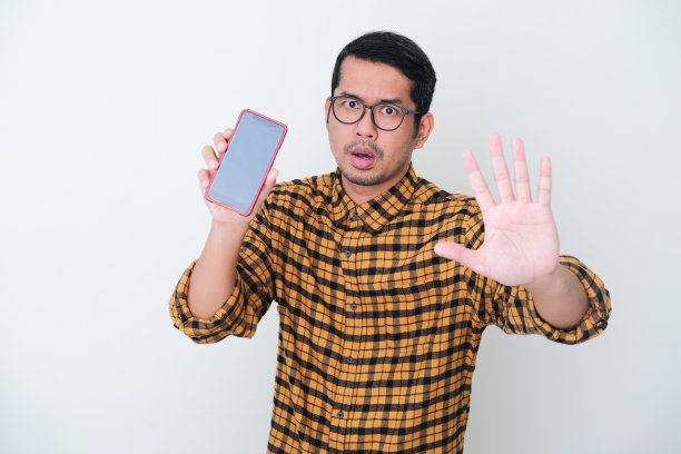 成年亚洲人穿着黄色法兰绒衬衫，在显示空白的手机屏幕时做手势停止图片下载