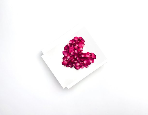 粉红色的心，玫瑰花瓣在白色的盒子上，白色的背景作为情人节贺卡的象征图片下载