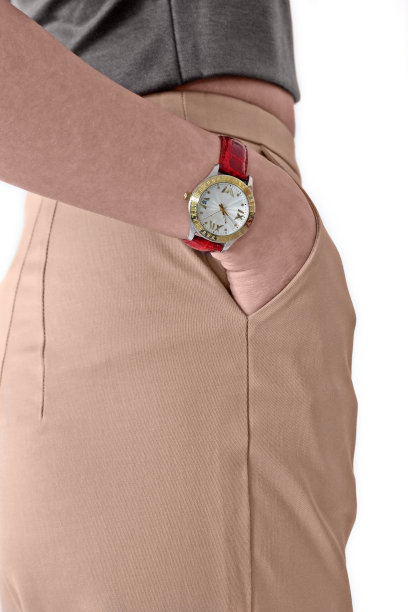 一个白人年轻女子侧身转过来，一只手握着一块手表。她穿着米色裤子和灰色上衣。图片下载