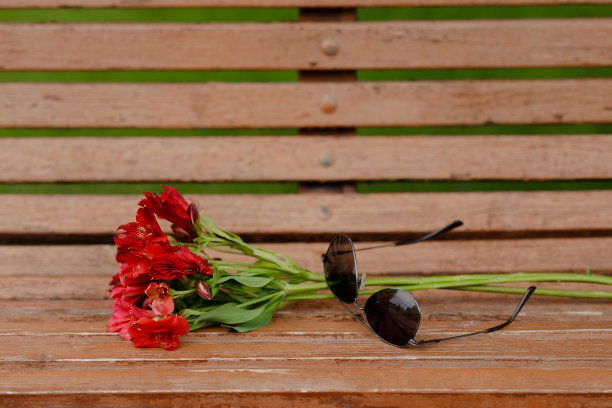 一张木凳上放着一副太阳镜和一束红花图片下载