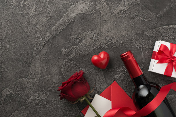 俯视图照片的情人节装饰葡萄酒酒瓶白色礼盒与红色蝴蝶结丝绸丝带心信封与红玫瑰在孤立的纹理深灰色混凝土背景与空白空间图片下载
