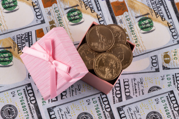 100美元纸币背景上印有1美元硬币的礼品盒图片下载