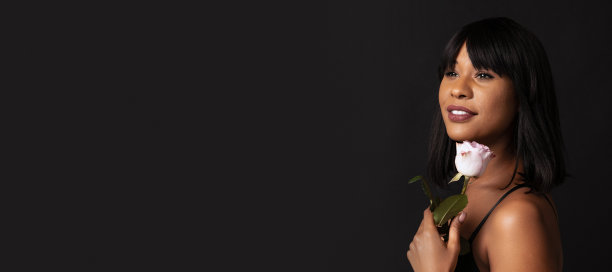特写漂亮的深色皮肤的女孩在黑色内衣与花孤立在黑暗的工作室背景。自然美景的概念。图片下载