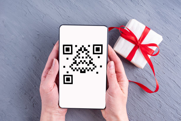 手拿着智能手机、平板电脑、带有二维码屏幕的手机，形状就像圣诞树和礼品盒图片下载