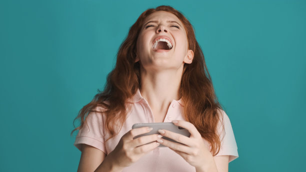 相当兴奋的红发女孩尖叫着，在智能手机上玩游戏，色彩丰富图片下载