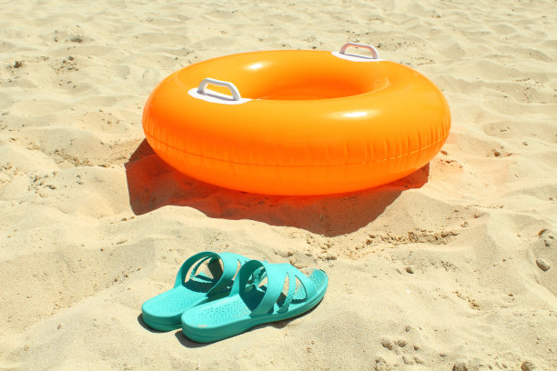 沙滩上的橙色游泳圈和蓝色女式板鞋图片下载