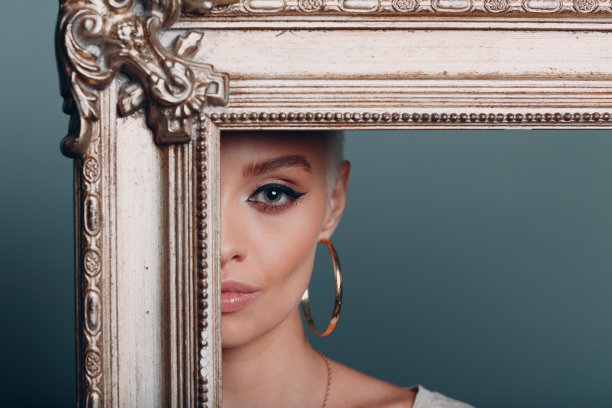 一名留着金色短发的千禧一代年轻女子，在她的头像后面，手里拿着一个镀金的相框。图片下载