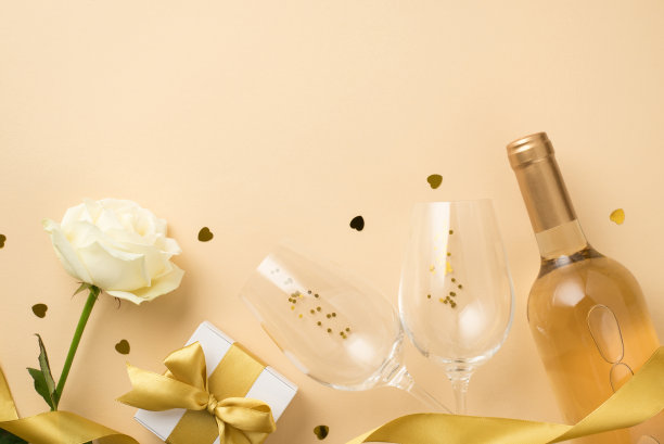 俯视图照片白玫瑰金丝带两个葡萄酒杯与金色亮片瓶白葡萄酒心形纸屑和白色礼盒与蝴蝶结孤立的米色背景与空白空间图片下载