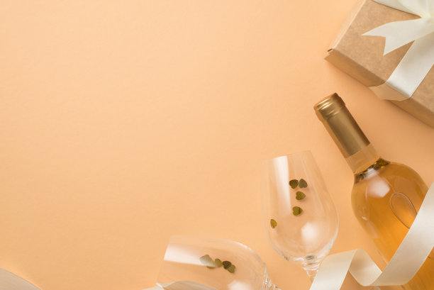 俯视图照片的情人节装饰葡萄酒酒瓶，葡萄酒杯与心形的彩纸丝绸丝带和牛皮纸礼盒白色蝴蝶结在孤立的粉彩米色背景与空空间图片下载