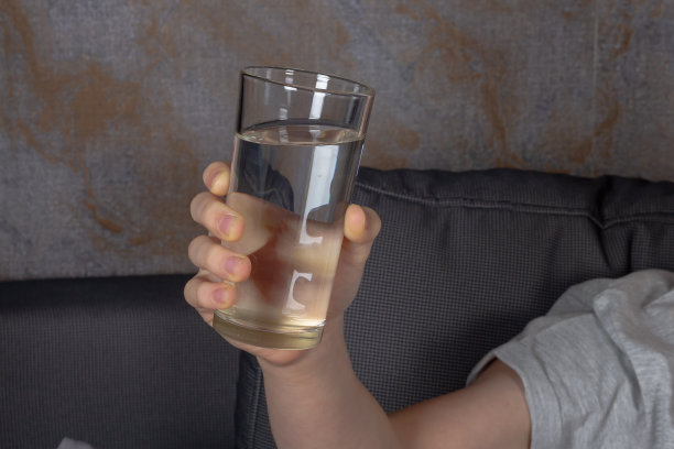 一个白人男孩坐在灰色的沙发上喝着杯子里的水图片下载