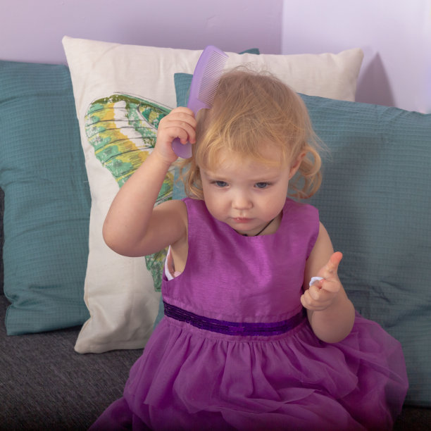 一个穿着漂亮紫色连衣裙的小女孩在她房间的沙发上用梳子梳头发图片下载