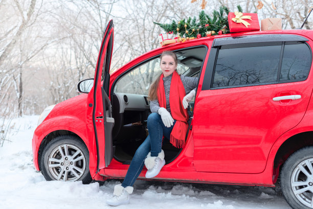 在圣诞节和寒假期间，美丽的年轻女子坐在为圣诞节装饰的红色轿车在冬季森林图片下载