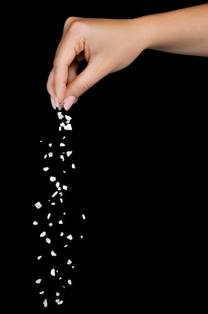 海盐从指尖落下，孤立在黑色上图片下载
