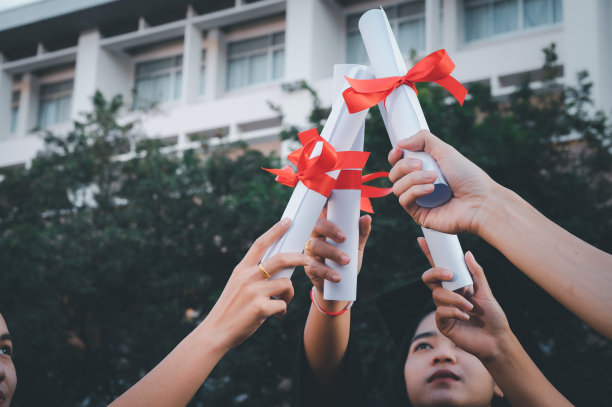 毕业生戴着黑帽子拿着大学毕业证书，向概念教育祝贺。毕业典礼，祝贺大学毕业生。图片下载