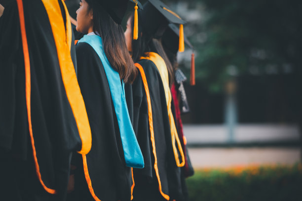 毕业生穿着传统的长袍和流苏帽站在夕阳下，手拿文凭，概念教育祝贺。毕业典礼，祝贺大学毕业生。图片下载