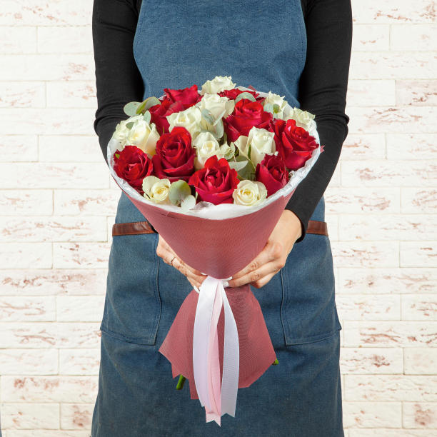 年轻的女花商穿着蓝色的围裙，拿着一束新鲜的红色花束，花束用纸包着，用丝带系在砖墙的背景上图片下载