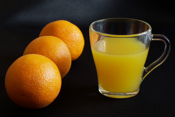三个新鲜的橙子和一个在深色表面上有橙汁的透明玻璃杯图片下载