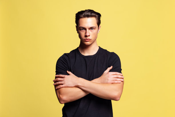 年轻英俊的肌肉男子的特写照片，穿着黑色t恤，看着镜头孤立在黄色的工作室背景。图片下载