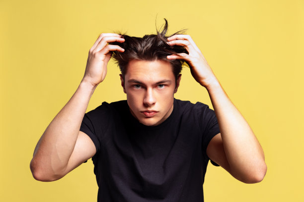 年轻英俊的男子与头发问题的半长肖像孤立在黄色工作室背景。图片下载