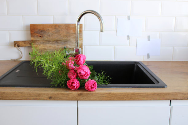 厨房内部的特写。白砖墙，地砖，带砧板的木制台面。黑色的水池里放着粉红色的牡丹。现代北欧设计。家居布置，清洁概念。图片下载