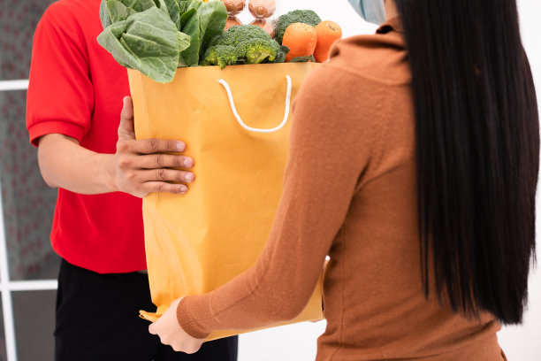 亚洲送货员从超市戴着口罩，拿着一袋新鲜的食物，蔬菜和水果给家里的顾客。速食服务理念与新生活方式图片下载