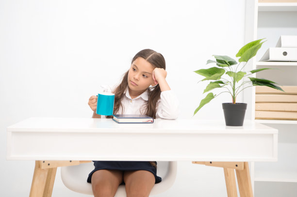 利用休息来放松。女孩抱着杯子坐在桌子白色的内部。一个女生在休息的时候喝茶。孩子校服梦幻脸捧杯。其余重要部分是教育过程图片下载