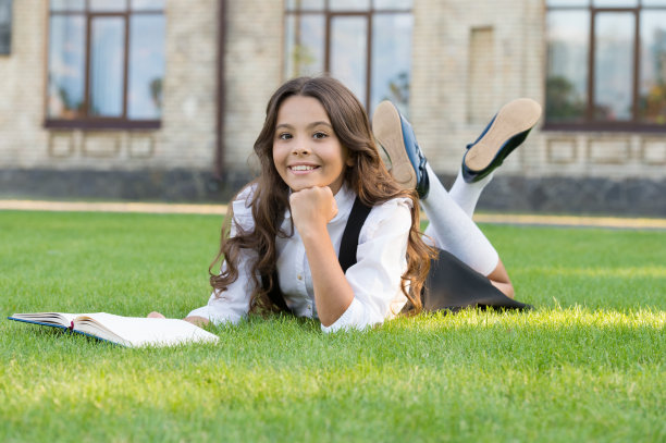 呼吸新鲜空气。可爱的小孩在户外看书。学习的概念。基础教育。教育的书。文学对孩子。女生校服躺在草坪上，手里拿着心爱的书图片下载
