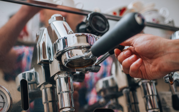 浓缩咖啡机上，新鲜的咖啡从闪亮的金属滤嘴倒入白色陶瓷杯的特写镜头图片下载