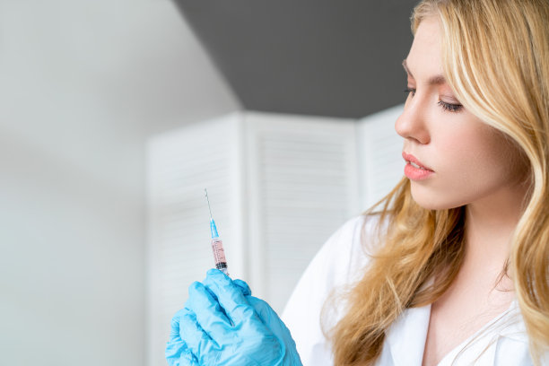 年轻漂亮的护士手持注射器，紧贴面部，自愿接种covid-19疫苗的概念。图片下载