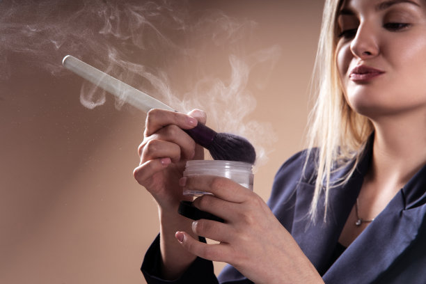 年轻的女化妆师，用刷子和粉化妆。粉在空气中。专业化妆的概念。撅起嘴唇和亲吻的姿势。图片下载