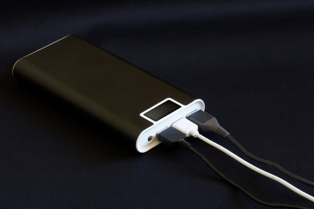 一个黑色的外部电池——一个带有显示器和三个USB接口的电源库——躺在黑暗的背景上。为许多小玩意儿充电的概念。为碑文留出空间图片下载
