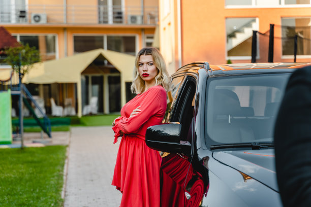 在夏日的户外，一名疯狂的白人成年女性穿着衣服，双手交叉，倚靠在汽车上，愤怒地看着镜头的侧面照片图片下载